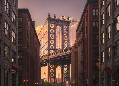 The Manhattan Bridge framed by brick buildings during sunset.