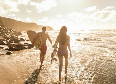 Two surfers walking along the beach at sunset with surfboards.
